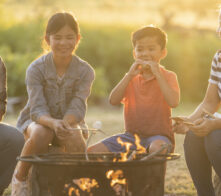 Asian family enjoying their time around a campfire while roasting and eating marshmallows while camping.